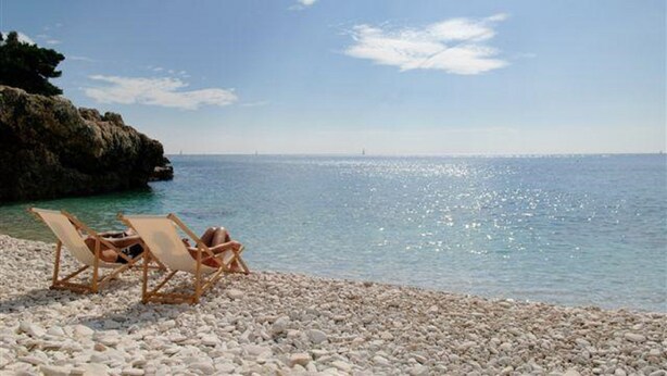 Una playa con dos sillones de madera mirando al mar, rodeada de piedras.