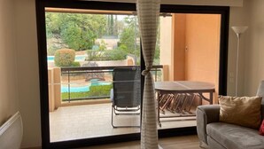 Een kamer met een schuifglasdeur die leidt naar een balkon met een zwembad, tuinmeubilair en uitzicht op groen.