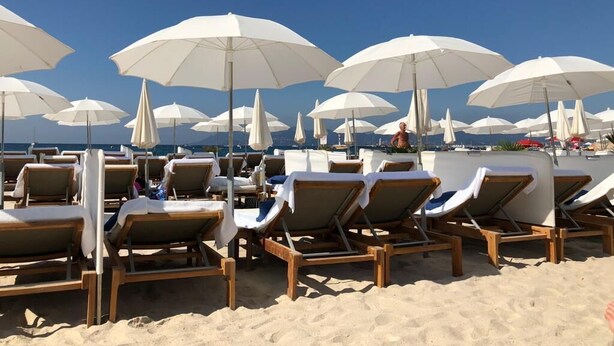 Een strand met rijen houten ligbedden en witte parasols, klaar voor een zonnebad.