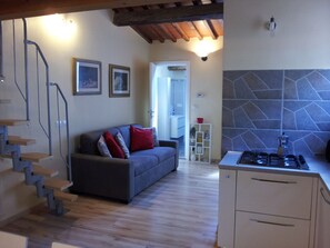 A modern living room with a grey sofa, red and silver cushions, a staircase, and a kitchen with a stone backsplash. - Residence MONNA LISA accommodates up to 7 people (Firenze)
