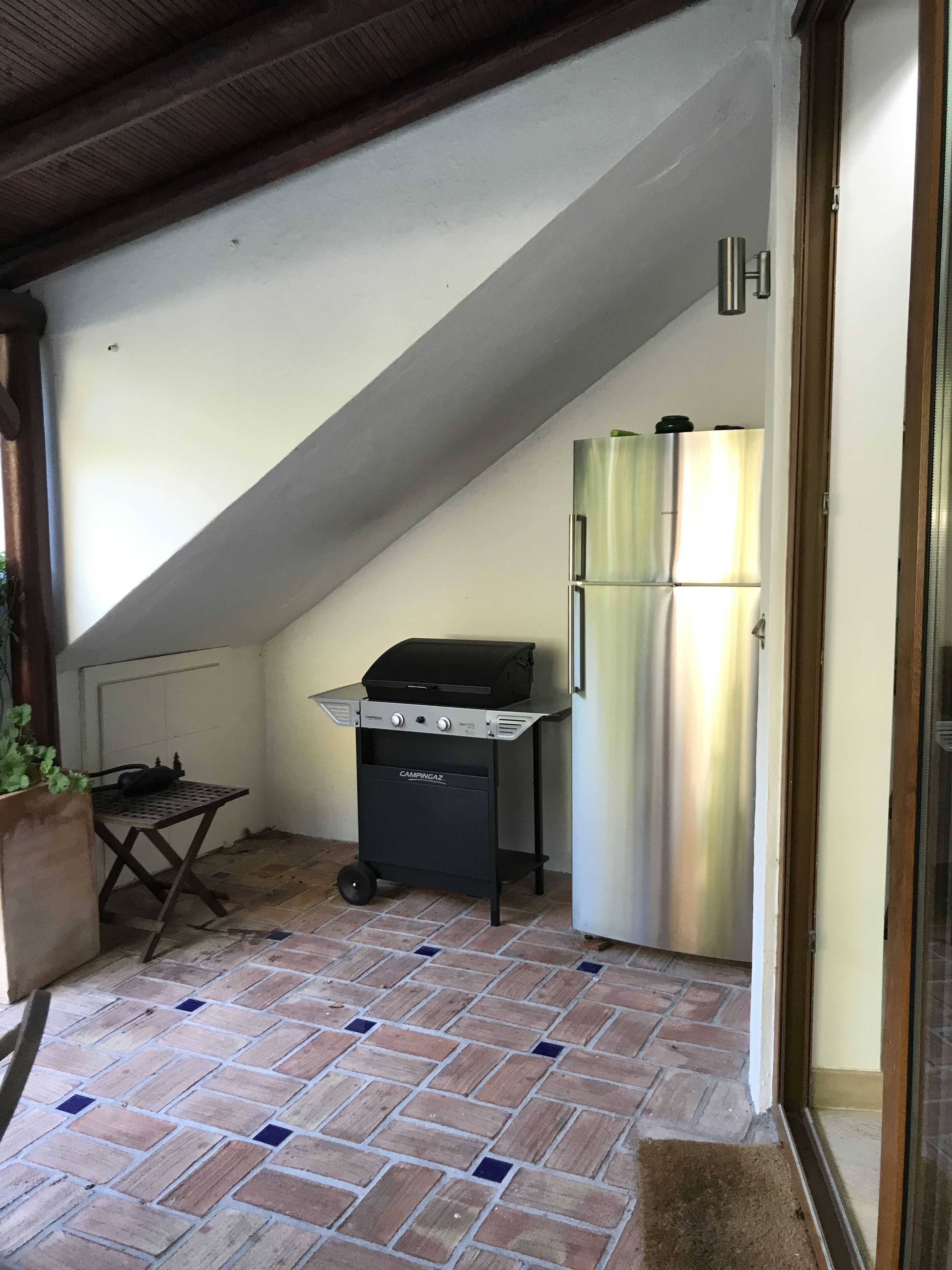A small kitchen with a grill, refrigerator, and tiled floor.