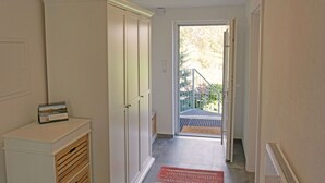 A hallway with a white wardrobe, a small table with a calendar, and a door leading to a balcony with a view of trees.