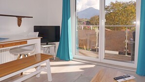 A modern living room with a TV, wooden bench, and a balcony with a view of a mountain and trees.