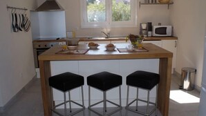 Une cuisine dotée d’un îlot central, de trois tabourets de bar noirs, d’un four à micro-ondes et d’une fenêtre donnant sur un paysage verdoyant.