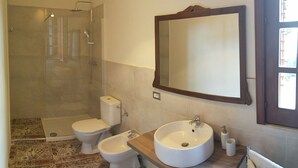 A bathroom with a shower, toilet, bidet, and sink.