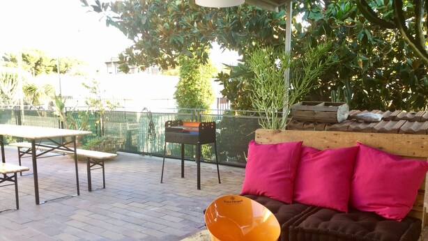 An outdoor patio area with a wooden bench, a table, and a cushioned seating area with pillows.