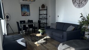 A modern living room with a sectional sofa, a dining table with chairs, a coffee table with a plant, and a wall clock. - Cocooning house - sea view - 4km from CANNES - 6 travellers (Golfe-Juan)