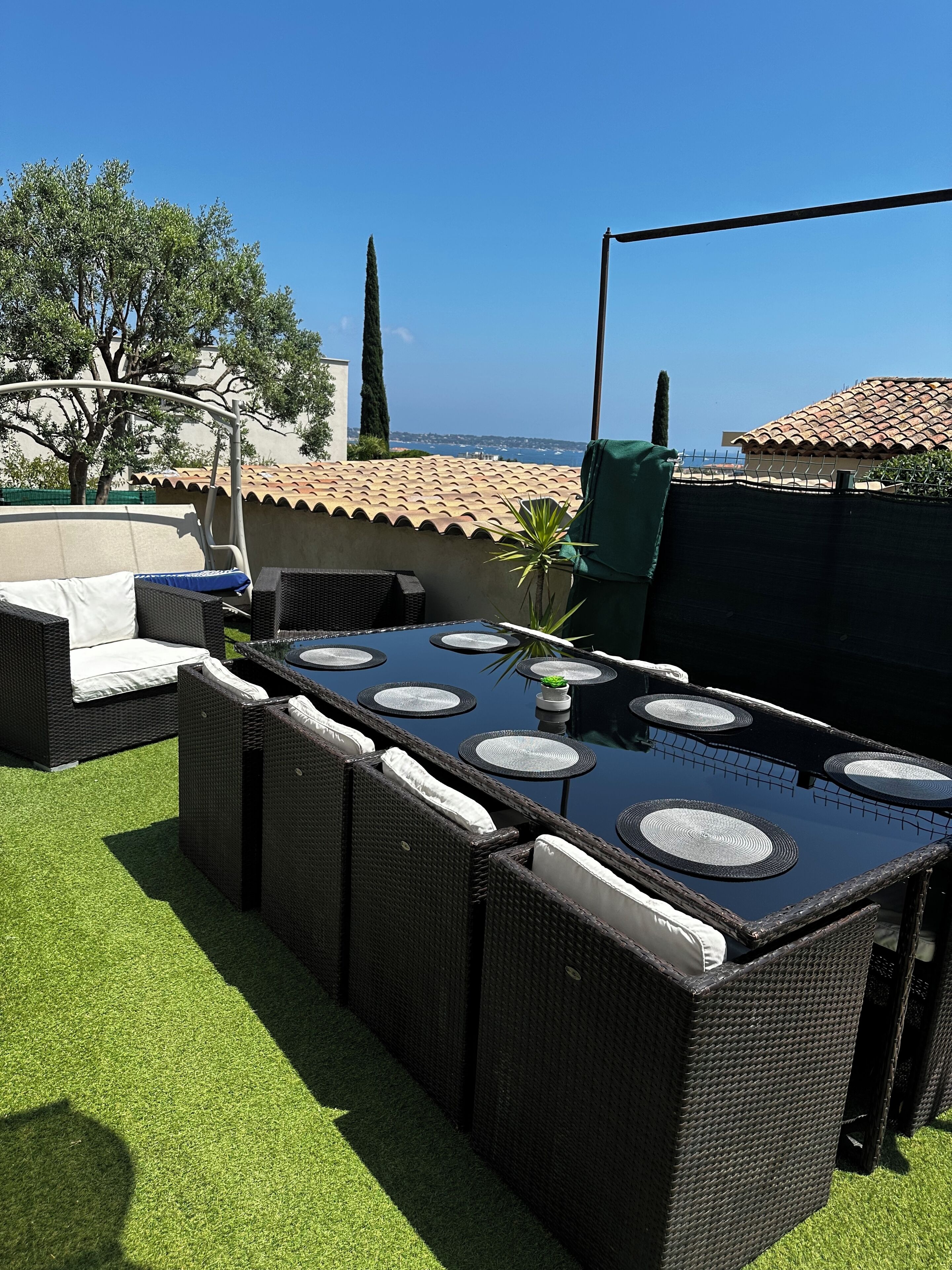 An outdoor patio with a long dining table, wicker furniture, and a view of the sea.
