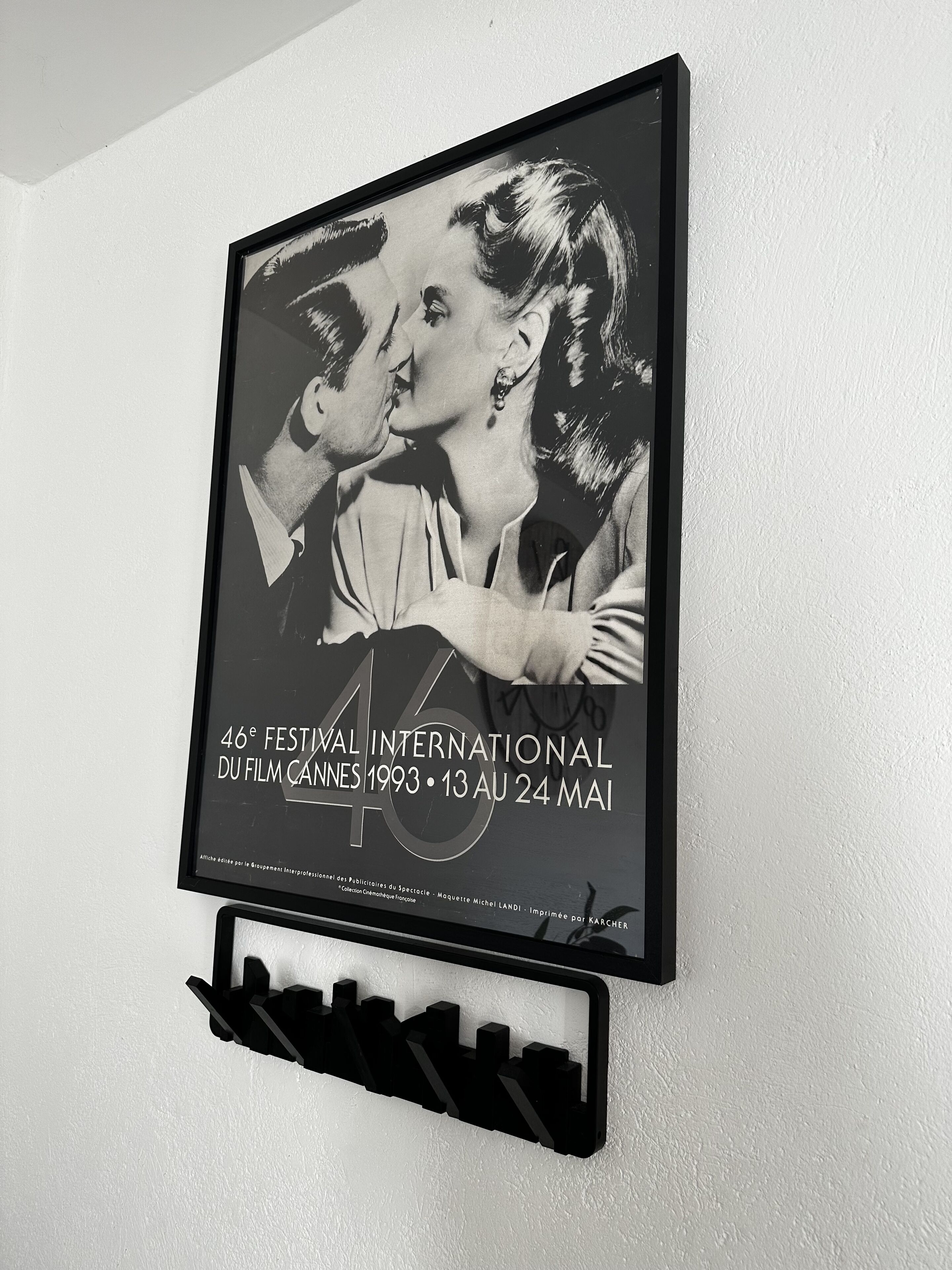 Een lijst met een zwart-witfoto van een koppel dat elkaar kust, hangend aan een witte muur met een zwarte voet eronder.