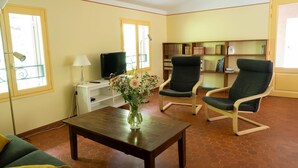 A living room with two chairs, a table, a TV, and a bookshelf. - Flat with loggia in a charming 18th century family estate, quiet, with independant entrance. (Hyères)