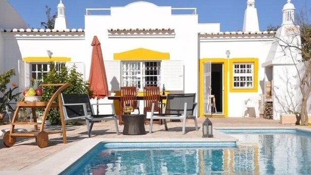A poolside area with a white building, yellow accents, and outdoor furniture. - Villa 500 meters from the sea with private saltwater pool in Meia Praia (Lagos)