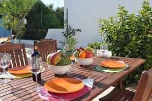 Een houten tafel gedekt voor een maaltijd, met schalen vol fruit, wijnkaraffen en borden.