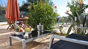 An outdoor seating area with a table set with fruits and a drink, surrounded by greenery and a decorative fountain. - Villa 500 meters from the sea with private saltwater pool in Meia Praia (Lagos)
