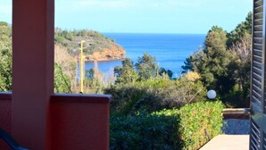 A coastal view from a balcony with a clear sky, a rocky shoreline, and dense greenery. - Casa Serena - SERENA E (Capoliveri)