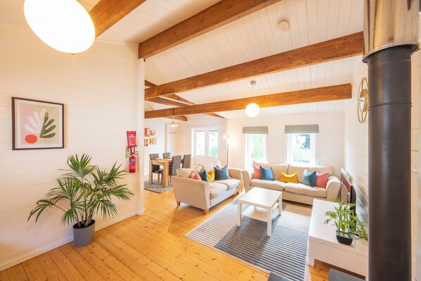 Un amplio salón con vigas de madera, una mesa de comedor, sofás y una chimenea.