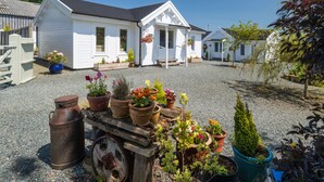 A white building with a porch, surrounded by gravel and potted plants.