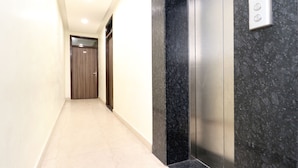 A hallway with a marble floor, a wooden door at the end, and an elevator with a digital display. - Hotel City Castle Prime (Amritsar)
