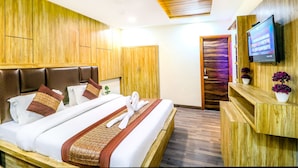 A hotel room with a wooden headboard, a bed with white bedding and decorative pillows, a wooden desk with a television, and a small plant. - Hotel City Castle Prime (Amritsar)