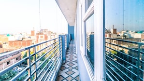 A narrow corridor with a tiled floor, metal railings, and large windows offering a view of the surrounding buildings. - Hotel City Castle Prime (Amritsar)