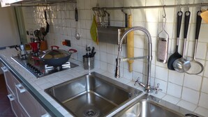 Ett kök med rostfria vitvaror, en dubbeldiskho och diverse köksredskap som hänger på väggen.