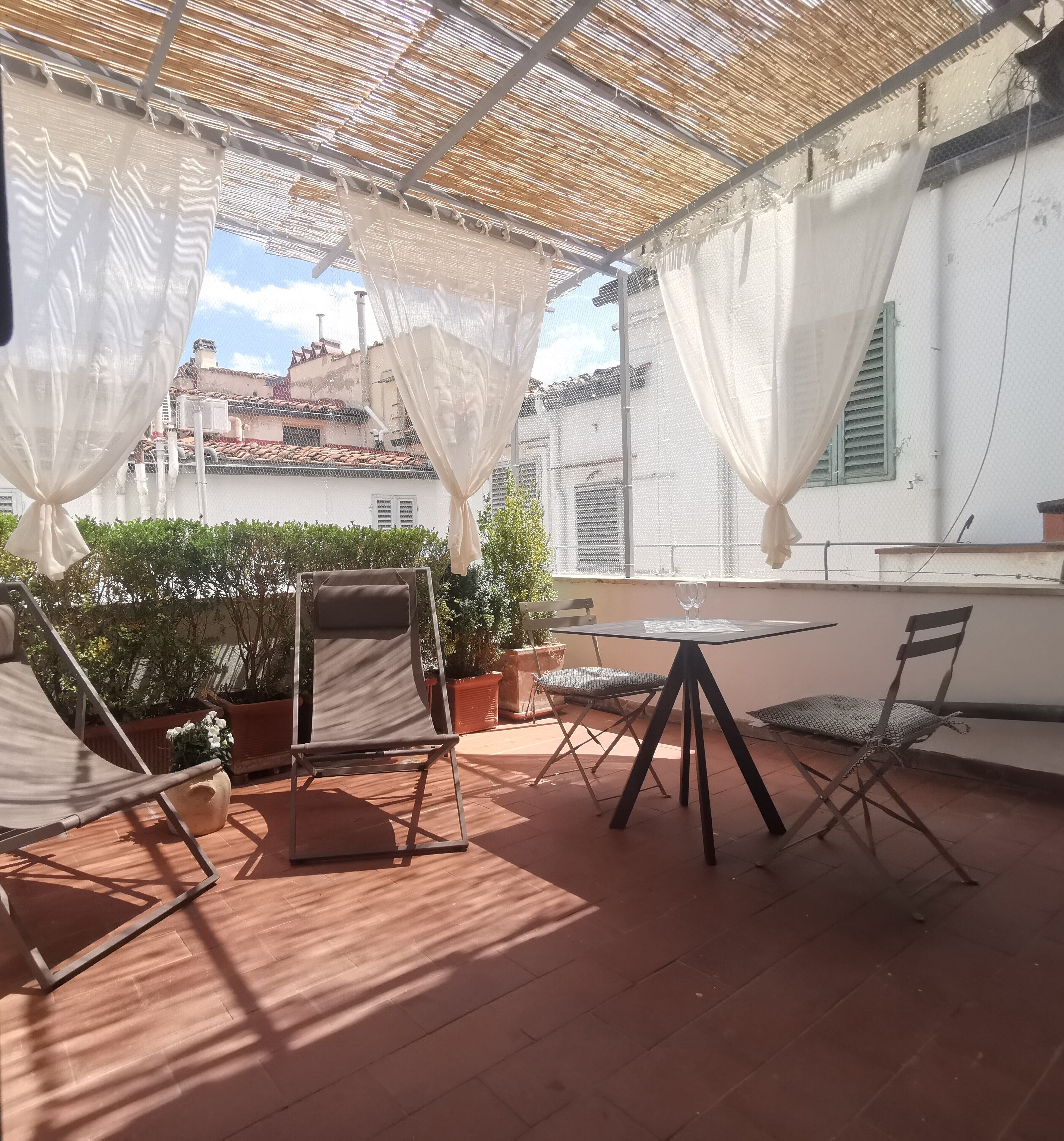 Un patio al aire libre con una mesa y sillas, una pérgola con cortinas blancas y plantas en macetas.