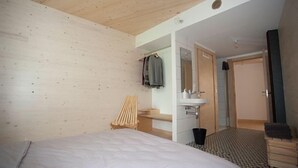 Et soveværelse med seng, træstol, lille skrivebord, spejl og badeværelse med håndvask og toilet.