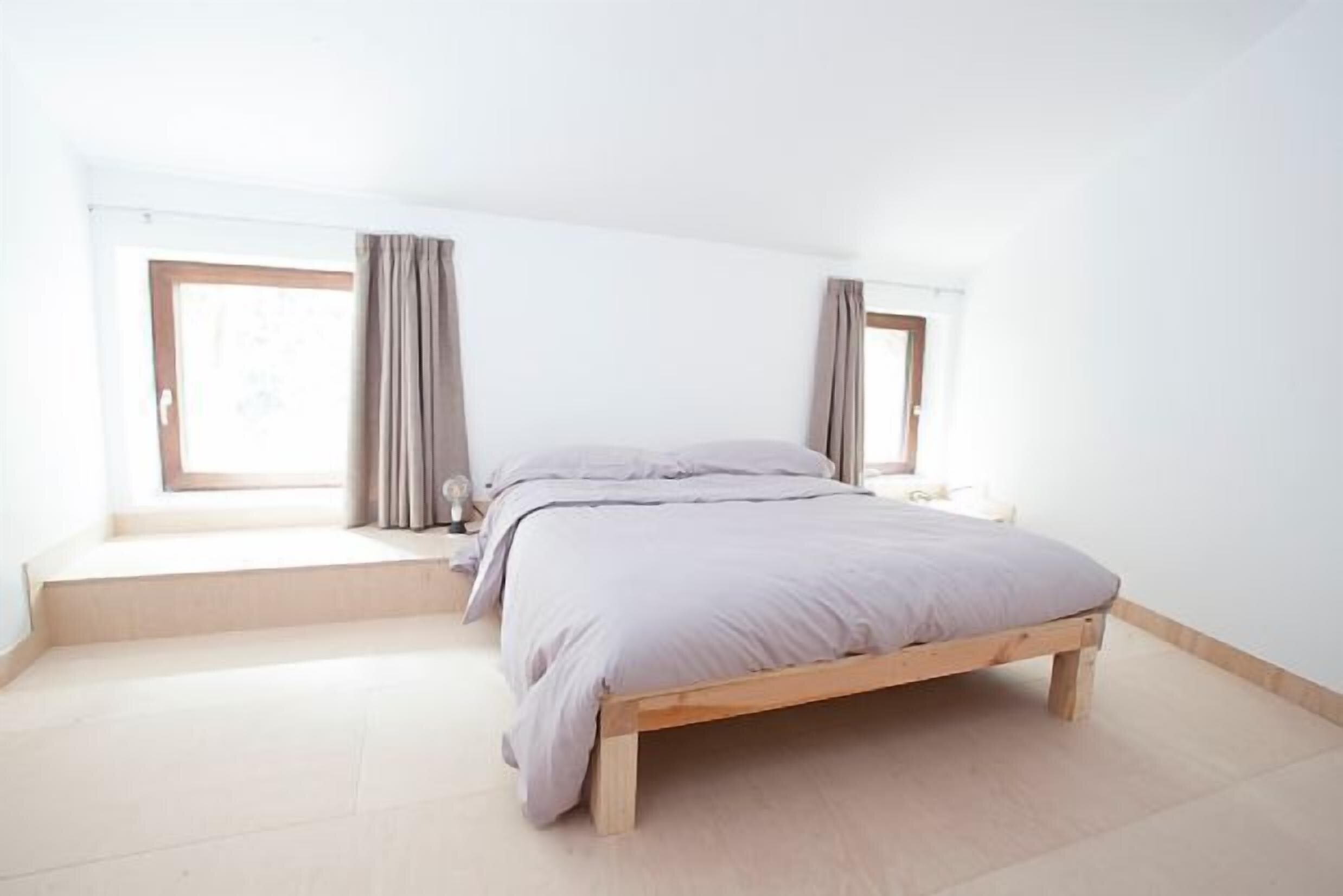 Une chambre à coucher avec un lit en bois, un banc près de la fenêtre et des rideaux.