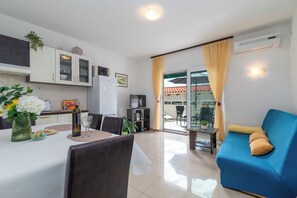 A modern living room with a blue sofa, a dining area with a table set for two, and a kitchen with white cabinets. - STIPE 2 with one bedroom, only 100m from the beach in Trogir (Trogir)
