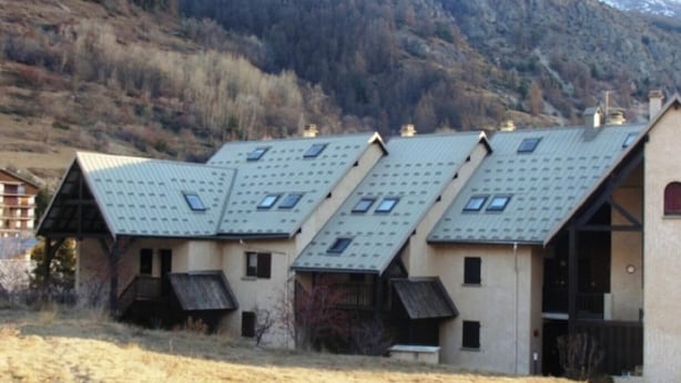 Une rangée de bâtiments de style chalet, avec des toits inclinés et de nombreuses fenêtres, se dressant sur un fond de montagnes.