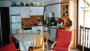 Une cuisine de taille réduite avec des meubles blancs, une table à manger avec des chaises et un fauteuil rouge recouvert de tissu.