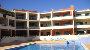 Ein mehrstöckiges Hotel mit Schwimmbad, Balkonen und Liegestühlen.