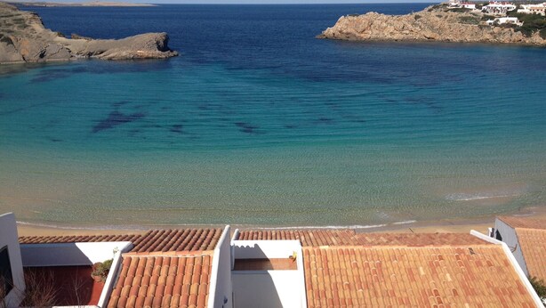 A coastal view with clear turquoise waters, rocky outcrops, and a white building with terracotta roof tiles. - 3 Bedroom Villa, private pool,  stunning Sea Views 5 mins from beach. WIFI & AC (Arenal D'en Castell)