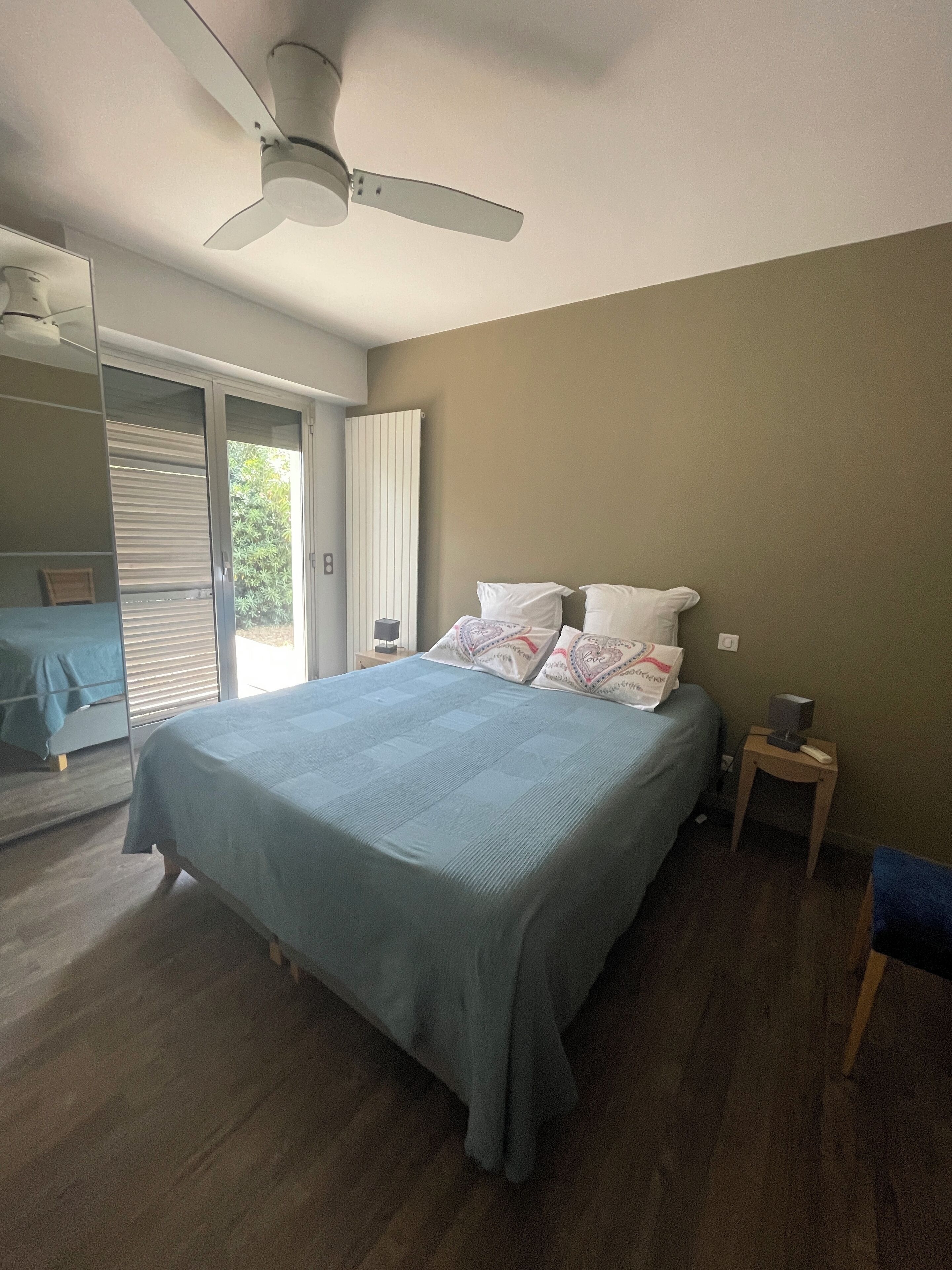 Een slaapkamer met een bed, een plafondventilator, een nachtkastje en uitzicht door een schuifdeur.