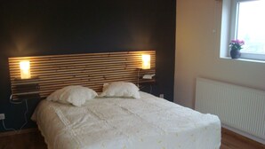 A bedroom with a wooden headboard, a bed with white bedding, and a window with a view of the outside. - Spacious and comfortable gîte with garden and very nice view  (Nassogne)