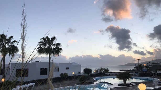 Un complexe hôtelier doté de plusieurs piscines, de palmiers et offrant une vue sur la mer au coucher du soleil.