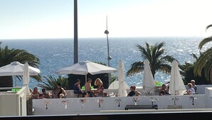 Un bar situé sur le toit, avec une terrasse, des parasols et une vue sur l’océan.