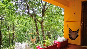 Un balcón con macetas rojas, una hamaca y vistas a un bosque.