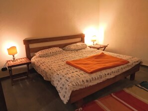 Ein ordentlich bezogenes Bett mit gemusterten Betttextilien, zwei Nachttischlampen und ein kleiner Holznachttisch.