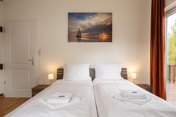 A hotel room with two beds, a painting of a sailboat on the wall, and a view of the outdoors through the window.