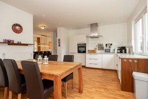 A modern kitchen with white cabinets, a wooden dining table, and a built-in oven.