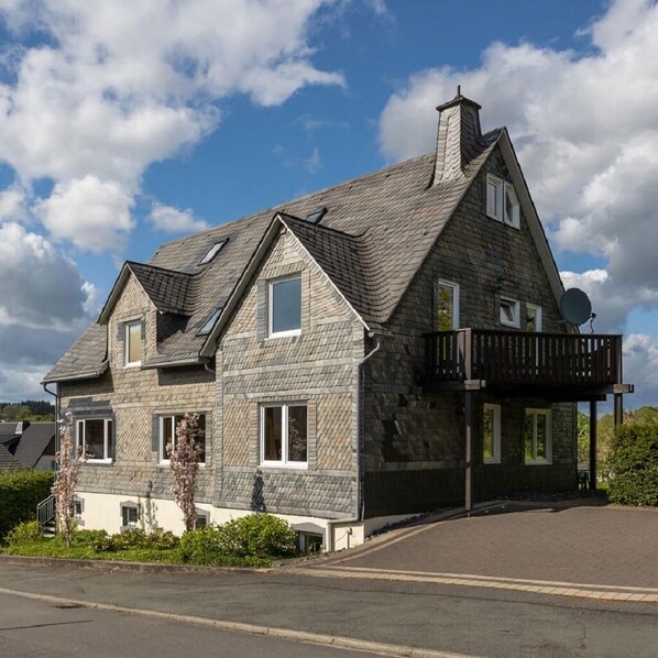 A two-story house with a stone facade, a balcony, and a satellite dish.