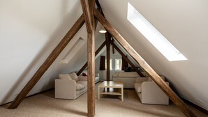 Een slaapkamer in loftstijl met een schuine plafond, zichtbare houten balken, een zithoek en een kleine tafel.