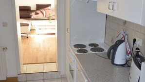 Een keuken met een kookplaat, waterkoker en een eethoek met een tafel en stoelen.