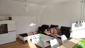 Een moderne woonkamer met een hoekbank, een witte salontafel en een eetgedeelte met een houten tafel en stoelen.