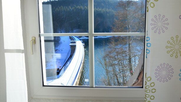 Een raam met uitzicht op een besneeuwd landschap, inclusief een weg en beboste heuvels.