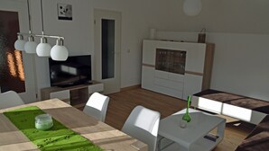 Een moderne woonkamer met een houten eettafel, witte stoelen, een witte bank en een televisie.