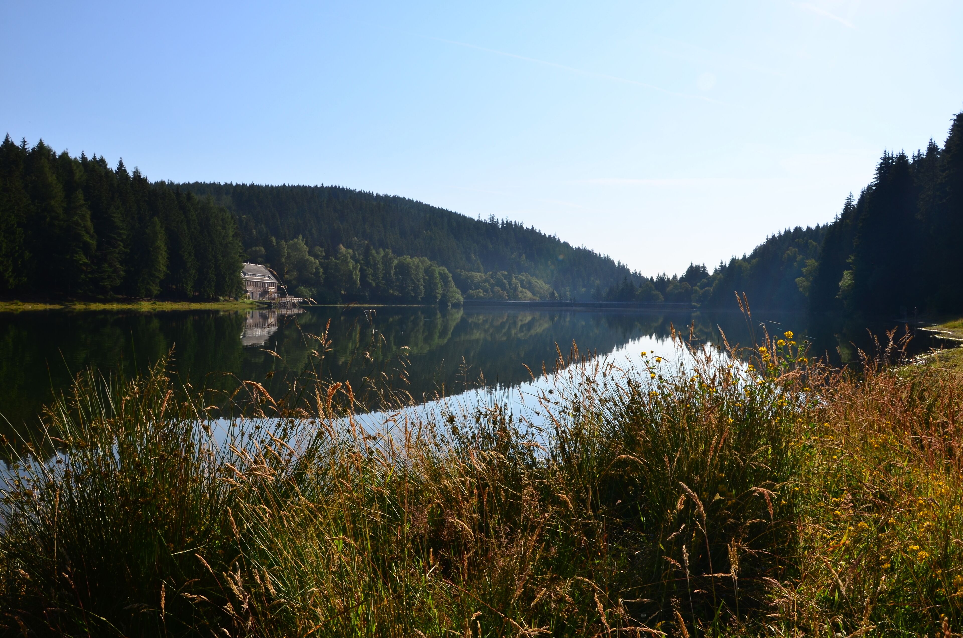 Un lago tranquilo con una casa a la izquierda y colinas boscosas al fondo.