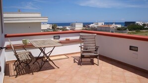 A rooftop terrace with a table and two chairs, a red railing, and a view of the sea and buildings in the distance. - Beautiful architect villa, sea views, WiFi (Torre Santa Sabina)