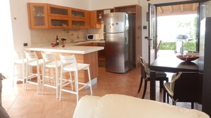A modern kitchen with a central island, bar stools, a refrigerator, and a dining table with chairs. - Beautiful architect villa, sea views, WiFi (Torre Santa Sabina)