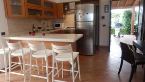 A modern kitchen with a central island, white chairs, and a stainless steel refrigerator. - Beautiful architect villa, sea views, WiFi (Torre Santa Sabina)